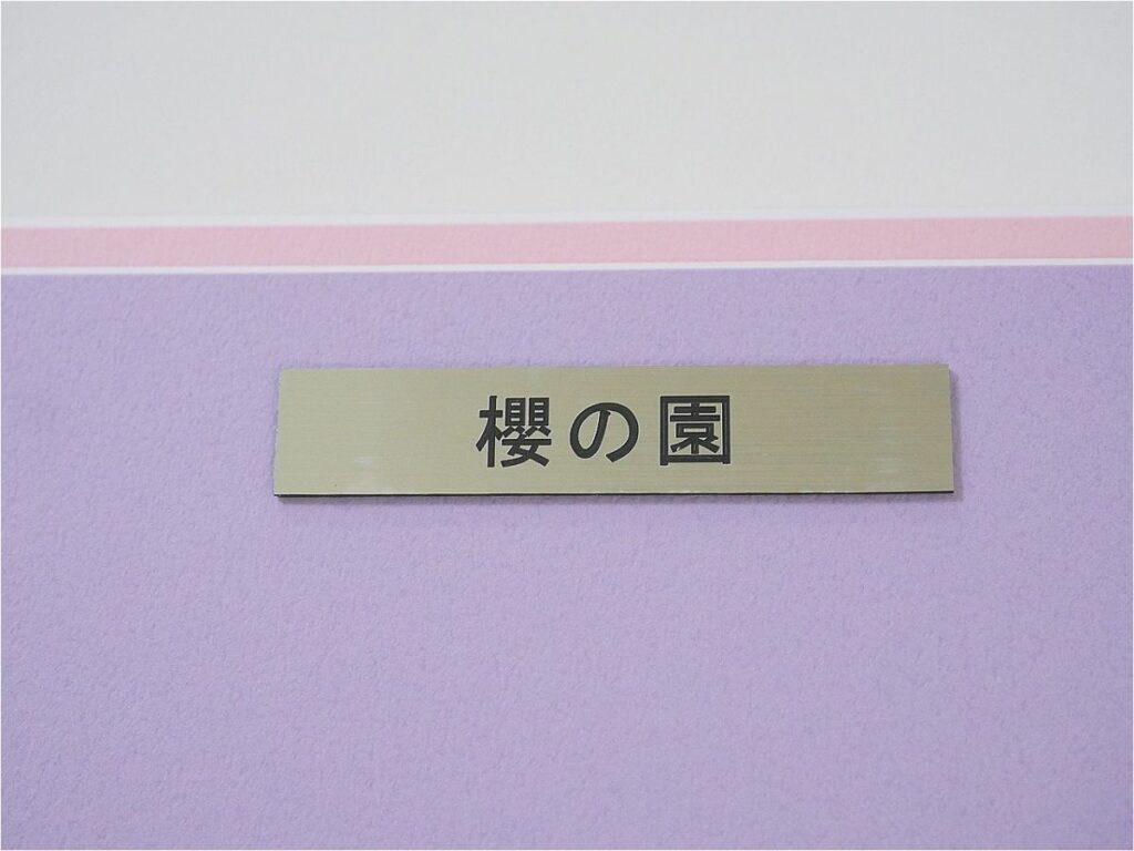 i-img1200x900-17724591075834hc3ukp273999 - 【絵巻本舗】二次元イラストグッズ特化型買取専門店 Beige rectangular plaque with black Japanese text 櫻の園 mounted on a lavender wall.