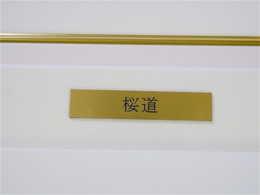 Gold rectangular nameplate with the Japanese characters "桜道" mounted on a pale wall.