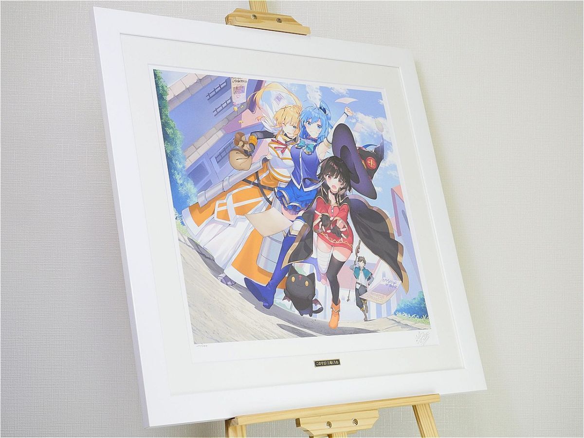 Framed anime illustration on a white mat resting on a wooden easel; a group of friends in colorful outfits walk outdoors, with a small black cat nearby.