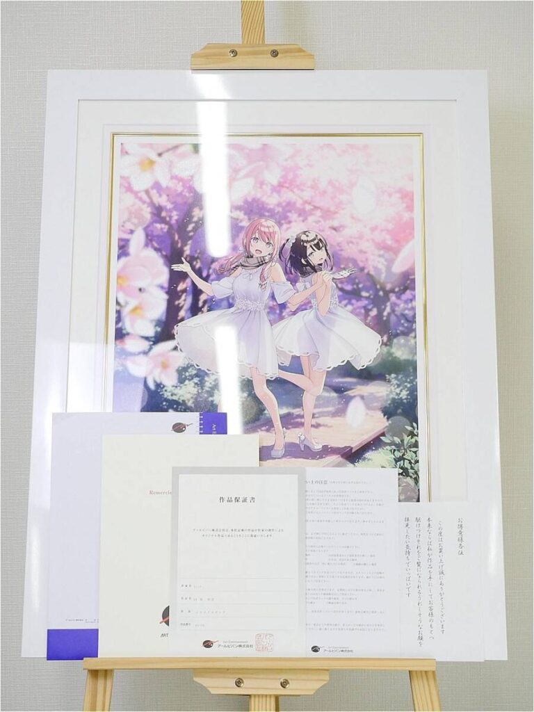 Framed anime artwork of two girls in white dresses posing under a pink cherry-blossom backdrop on an easel, with papers in front.