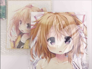 Two glossy anime posters featuring a young girl with orange hair and purple eyes; the front poster is partially wrapped in plastic, with a second poster visible behind it.